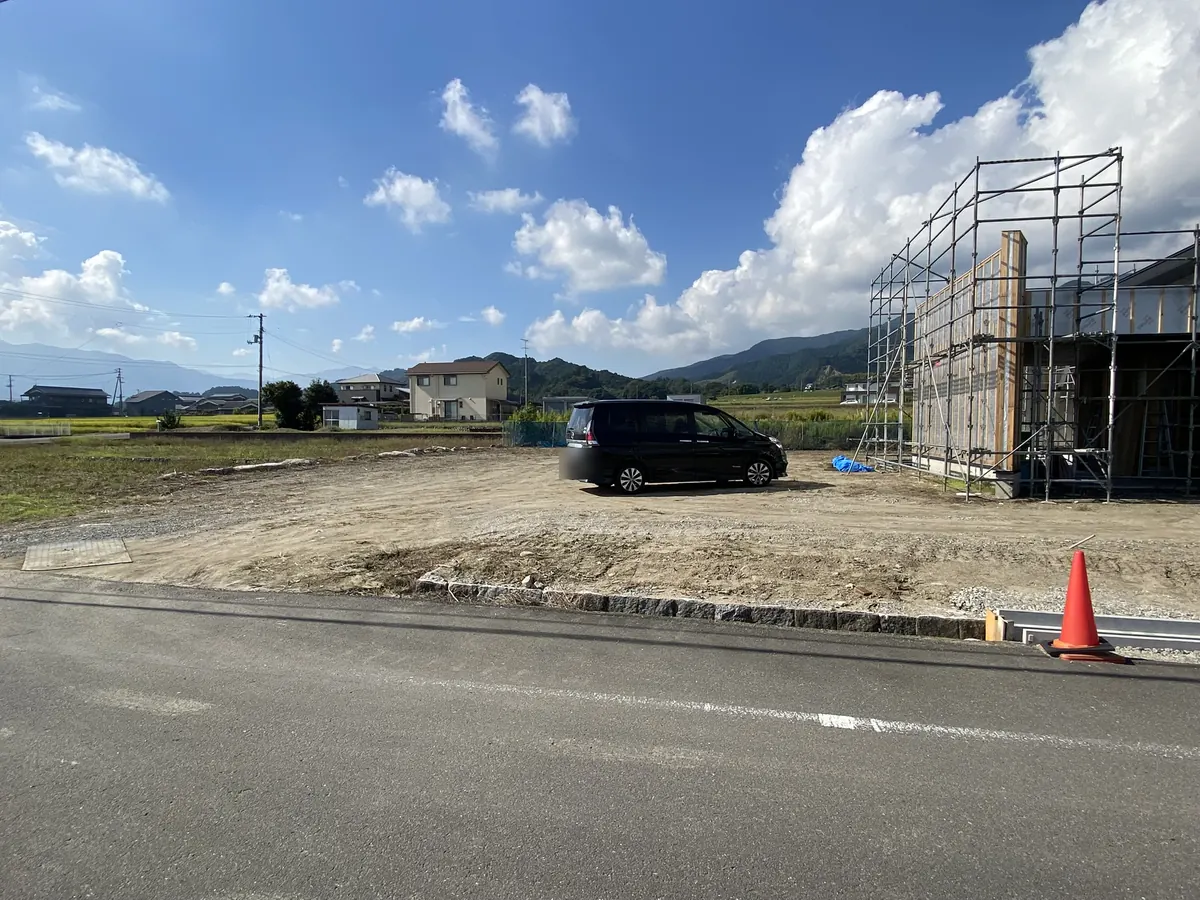 建築中の家の隣にある、砂利敷きの空き地の昼間の様子