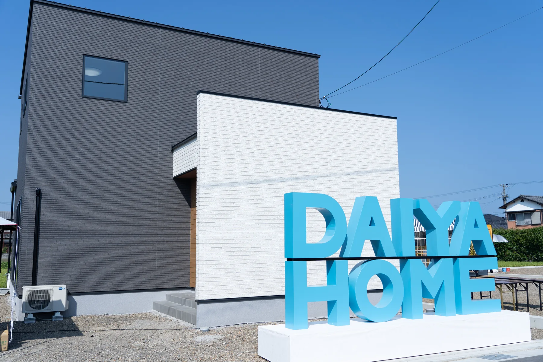 白と黒の住宅前に設置された青いDAIYAHOMEロゴ