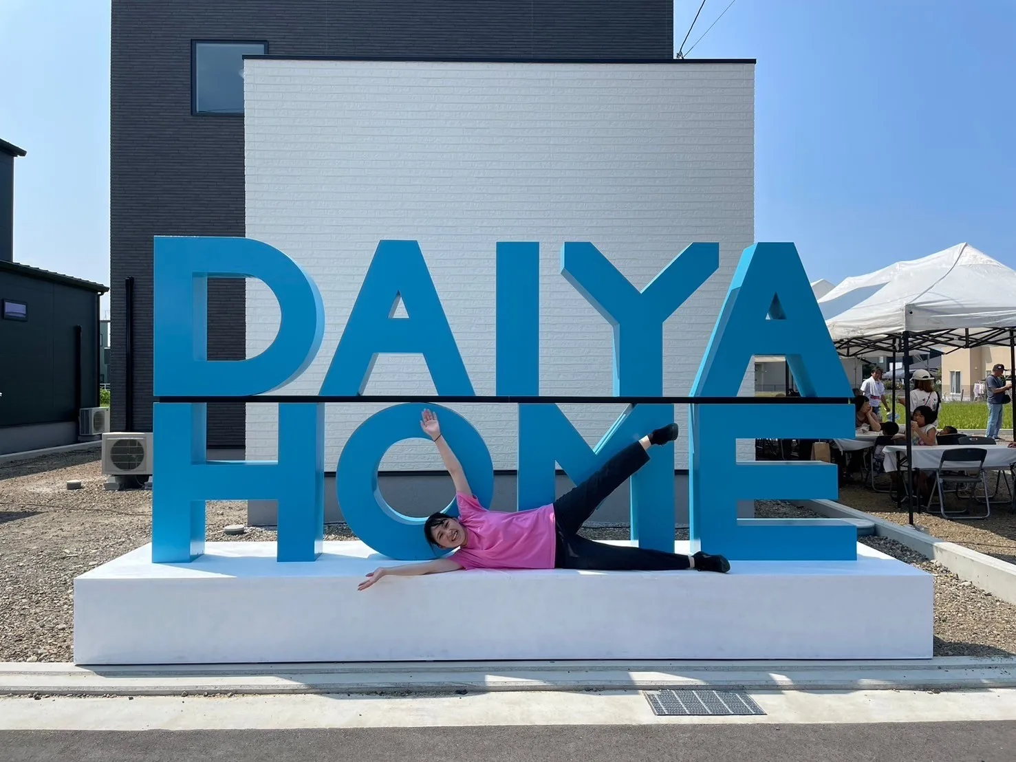 青いDAIYAHOMEロゴと一緒にポーズを取るイベント参加者