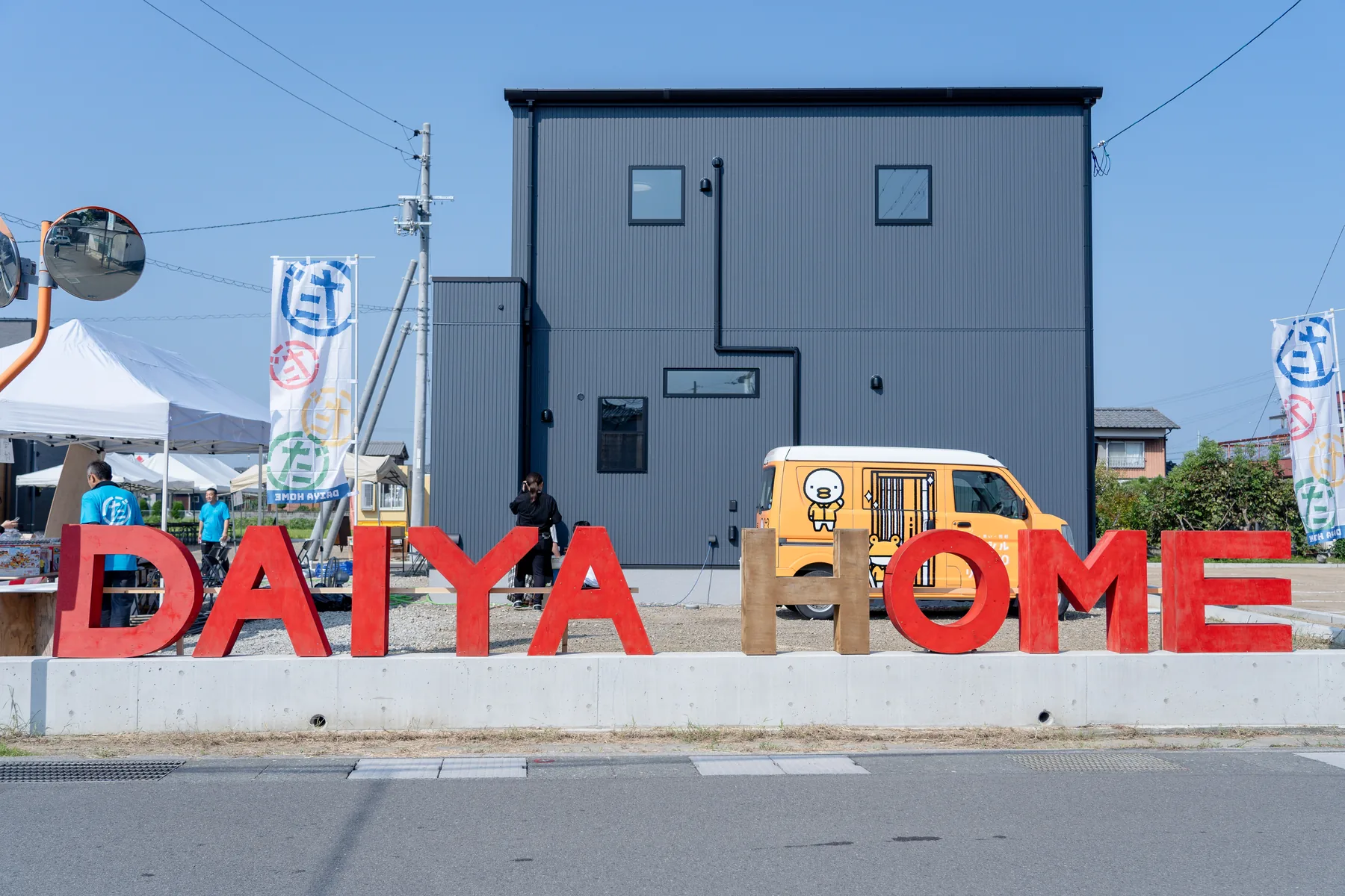 黒い住宅前に設置された赤と木目のDAIYAHOMEロゴ