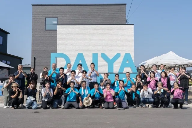 青いDAIYAHOMEロゴ前で集合写真を撮る地域イベント参加者