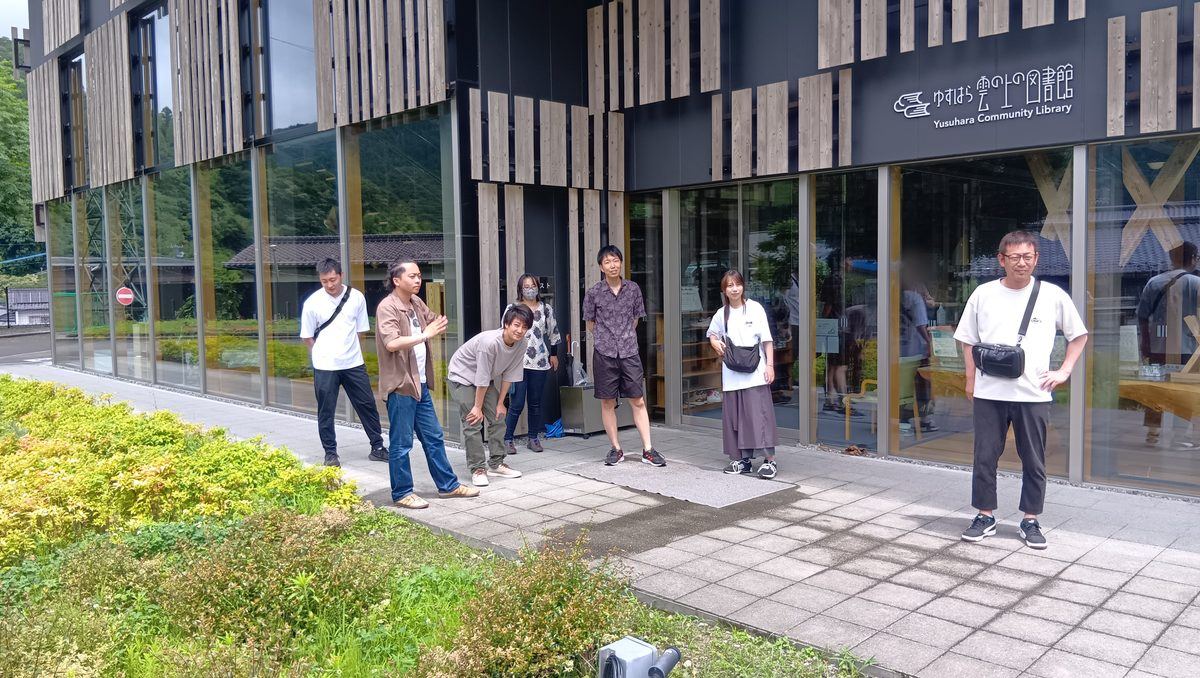 建物探訪ツアーで高知県梼原町の木造建築を見学するDAIYAHOMEのスタッフたち。木のルーバーとガラス張りの外観をもつ雲の上の図書館の前に立っている