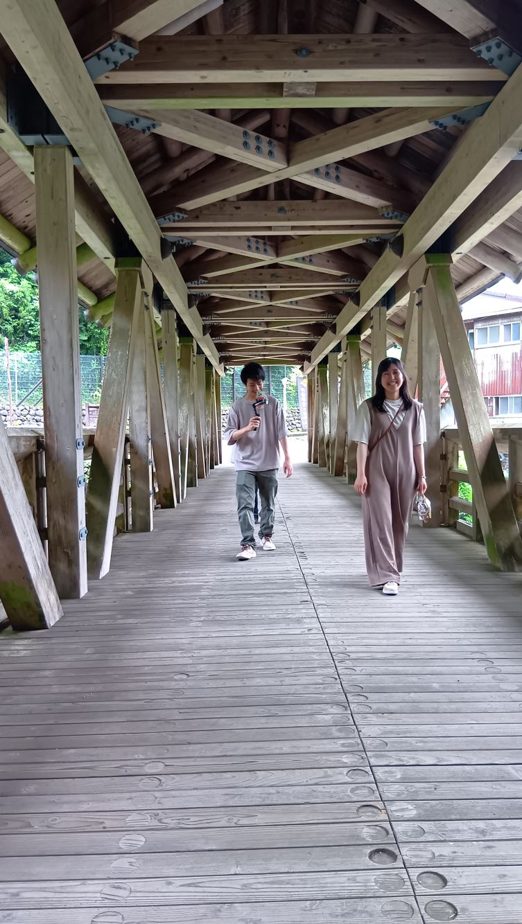 高知県梼原町・三嶋神社の屋根付き参道橋を渡るDAIYAHOMEのスタッフ2人。木の小屋組が連続する
