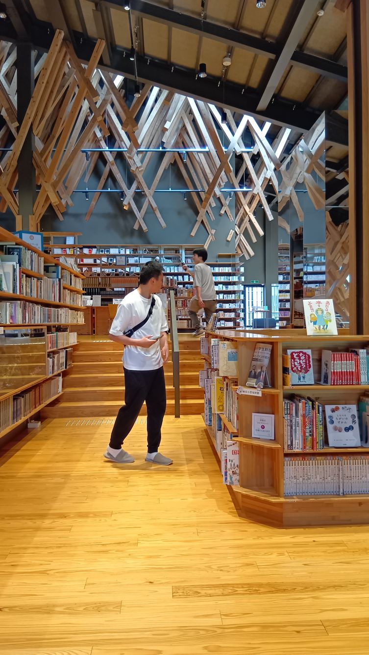 雲の上の図書館の本棚のあいだに立ち、天井に広がるスギの組木を見上げるDAIYAHOMEのスタッフ