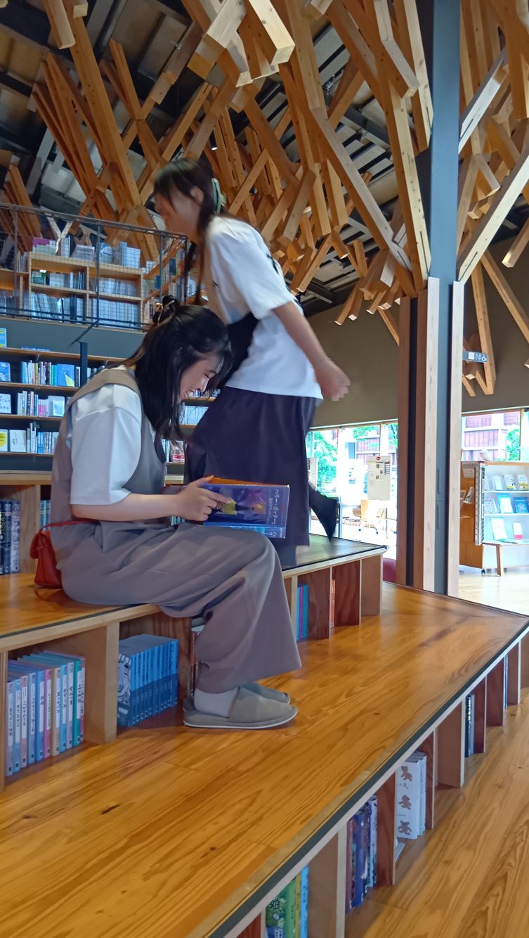 雲の上の図書館の階段状の床に腰掛けて本を開くスタッフ。段差の下がそのまま本棚になっている