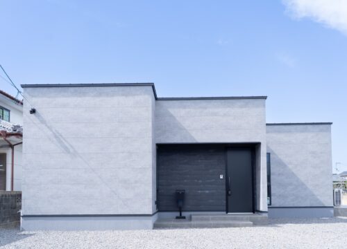 愛媛県新居浜市に建てた平屋の注文住宅の外観。ケイミューQFフィエルテ「チタン ダークコンクリート」のグレー外壁を大きな面で見せ、玄関まわりだけSOLID鉄黒を差し込んだシンプルモダンな佇まい