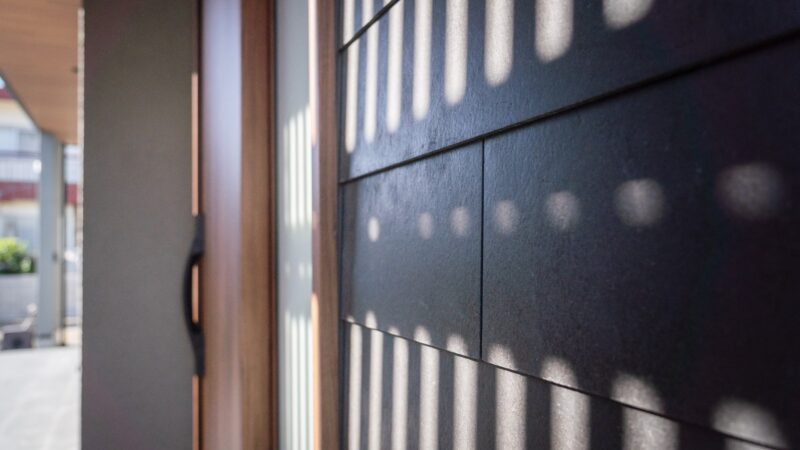 玄関まわりの外壁に落ちる格子の光。黒いアクセント外壁SOLID鉄黒の陰影が時間とともに変化する