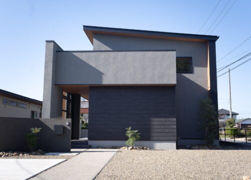 愛媛県新居浜市の2階建て注文住宅の正面外観。グレーの塗り壁と黒いアクセント外壁SOLID鉄黒、木製格子と門柱を組み合わせたジャパンディデザイン