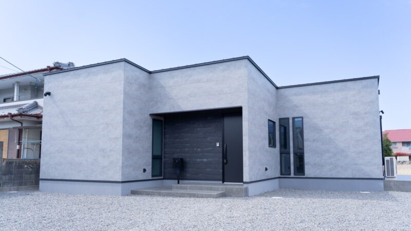 愛媛県新居浜市に建てた平屋の注文住宅の外観。ケイミューQFフィエルテ「チタン ダークコンクリート」の大判グレー外壁に、玄関まわりだけSOLID鉄黒を差し込んだシンプルモダンな佇まい
