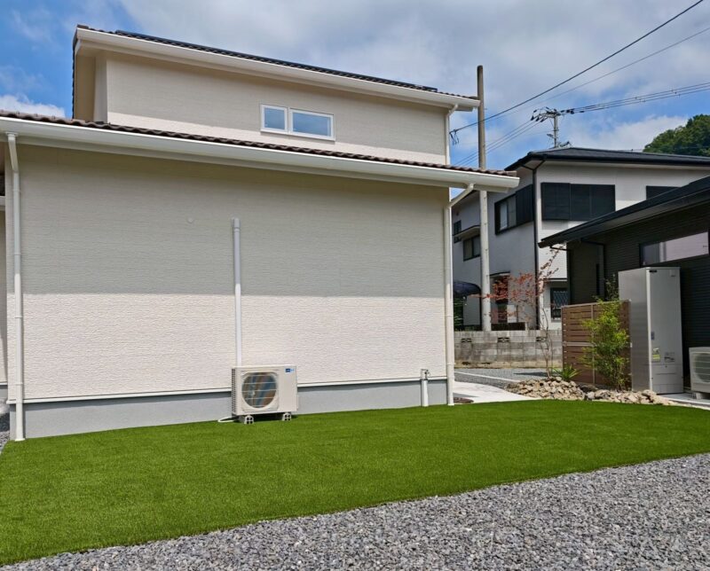 段違いの瓦屋根が重なる建物側面。白い外壁と人工芝の庭のコントラスト