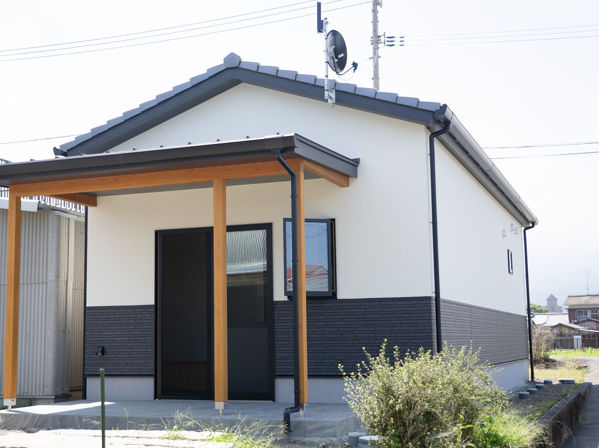 愛媛県西条市の和風平屋の外観。切妻屋根に大きな庇屋根を重ね、白い塗り壁調の外壁と黒い腰壁でまとめた住まい