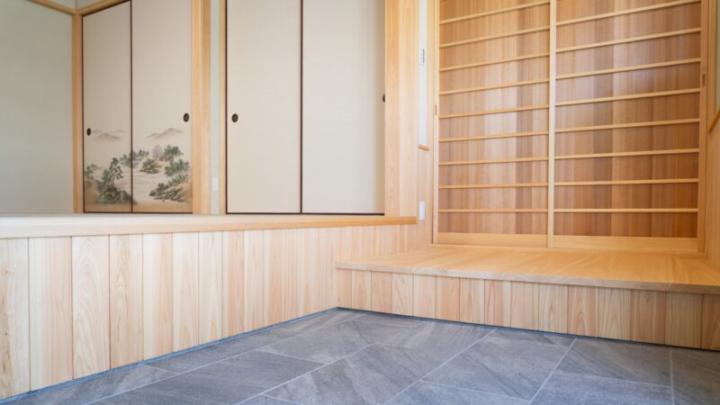 西条市の和風平屋の土間。桧の腰板張りと石調タイルを合わせ、山水画の襖と桧の格子戸が並ぶ和の設え