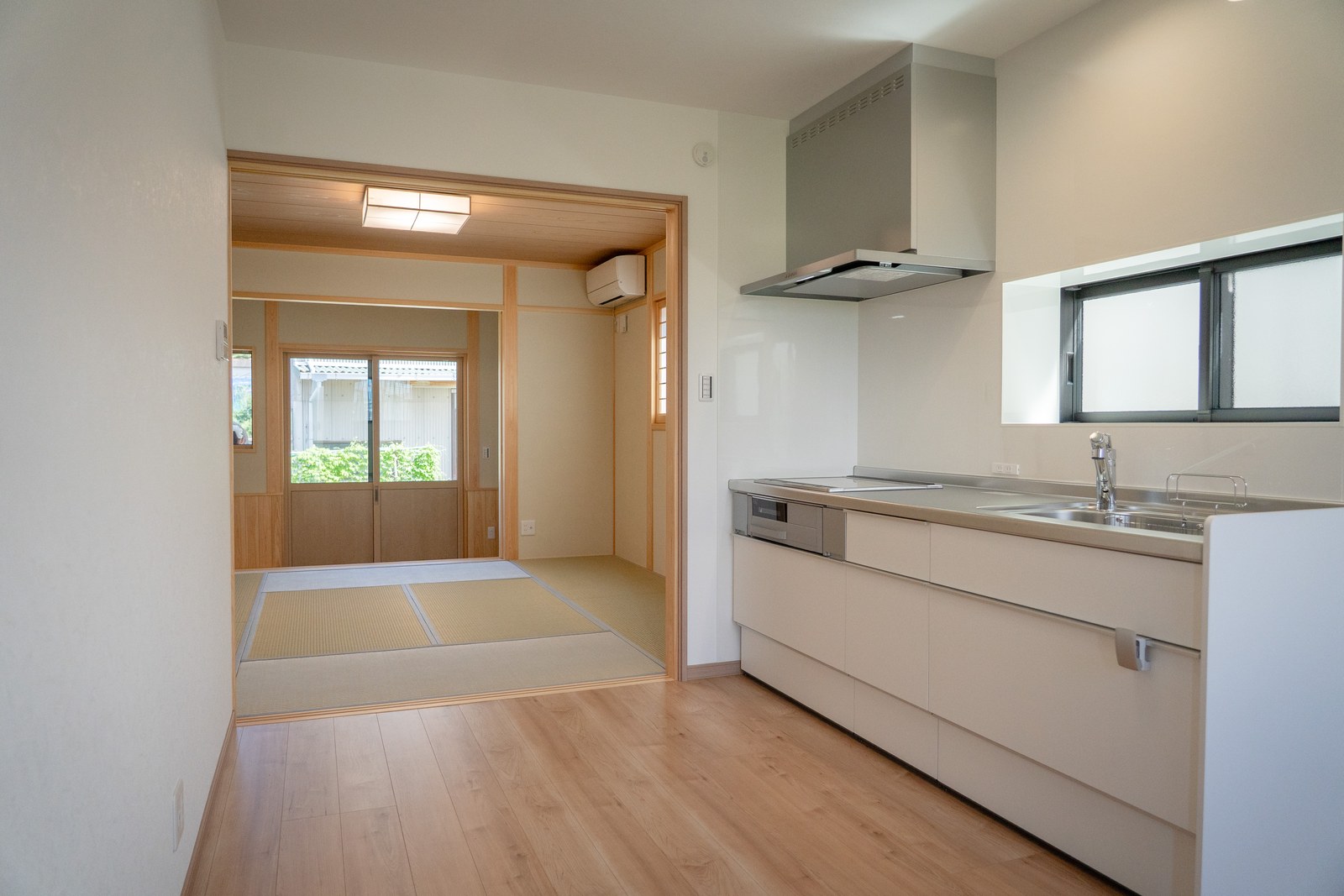 西条市の平屋のダイニングキッチンから和室を見たところ。建具を入れず、天井まで抜けた大きな開口でつないでいる